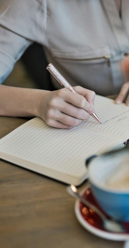 Woman writing in a notebook with a laptop and coffee cup on a desk. Ideal for workspace inspiration.