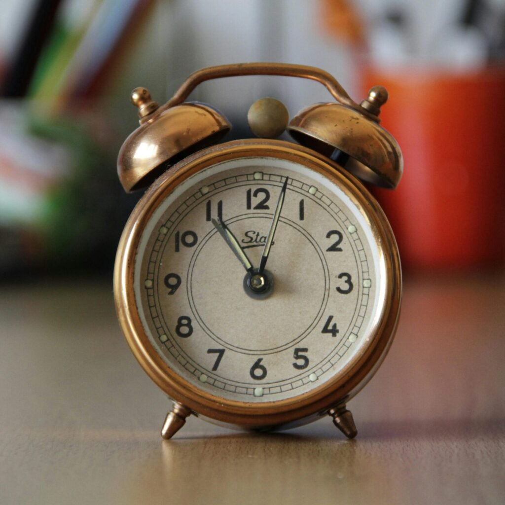 A vintage copper alarm clock with bells placed on a desk with blurred objects in the background.
