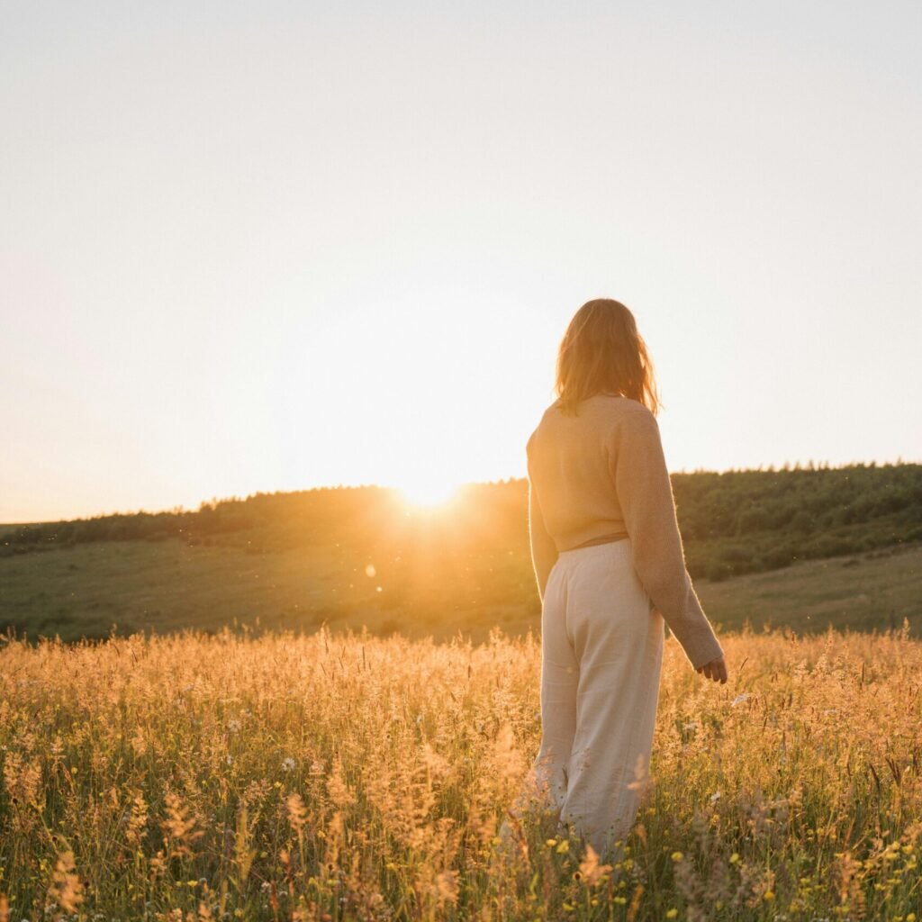 A tranquil moment of a woman in a summer meadow at sunset, capturing natural beauty and serenity.