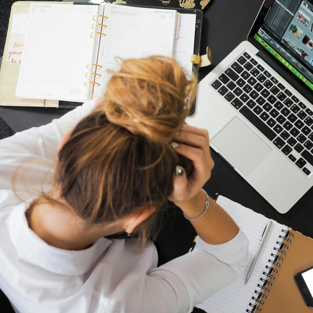 Overhead view of a stressed woman working at a desk with a laptop, phone, and notebooks.