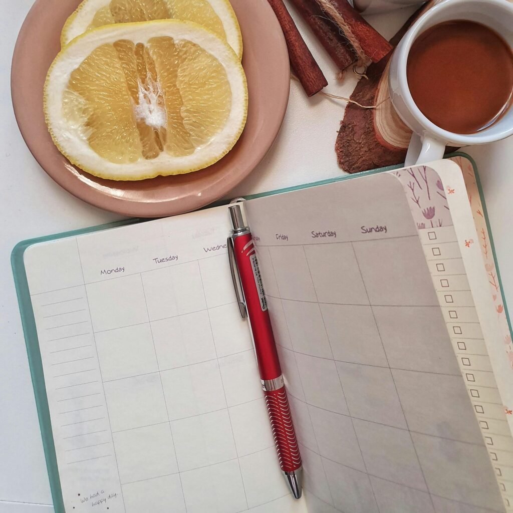 Flat lay of morning essentials including coffee, grapefruit, planner, and candle on a white table.