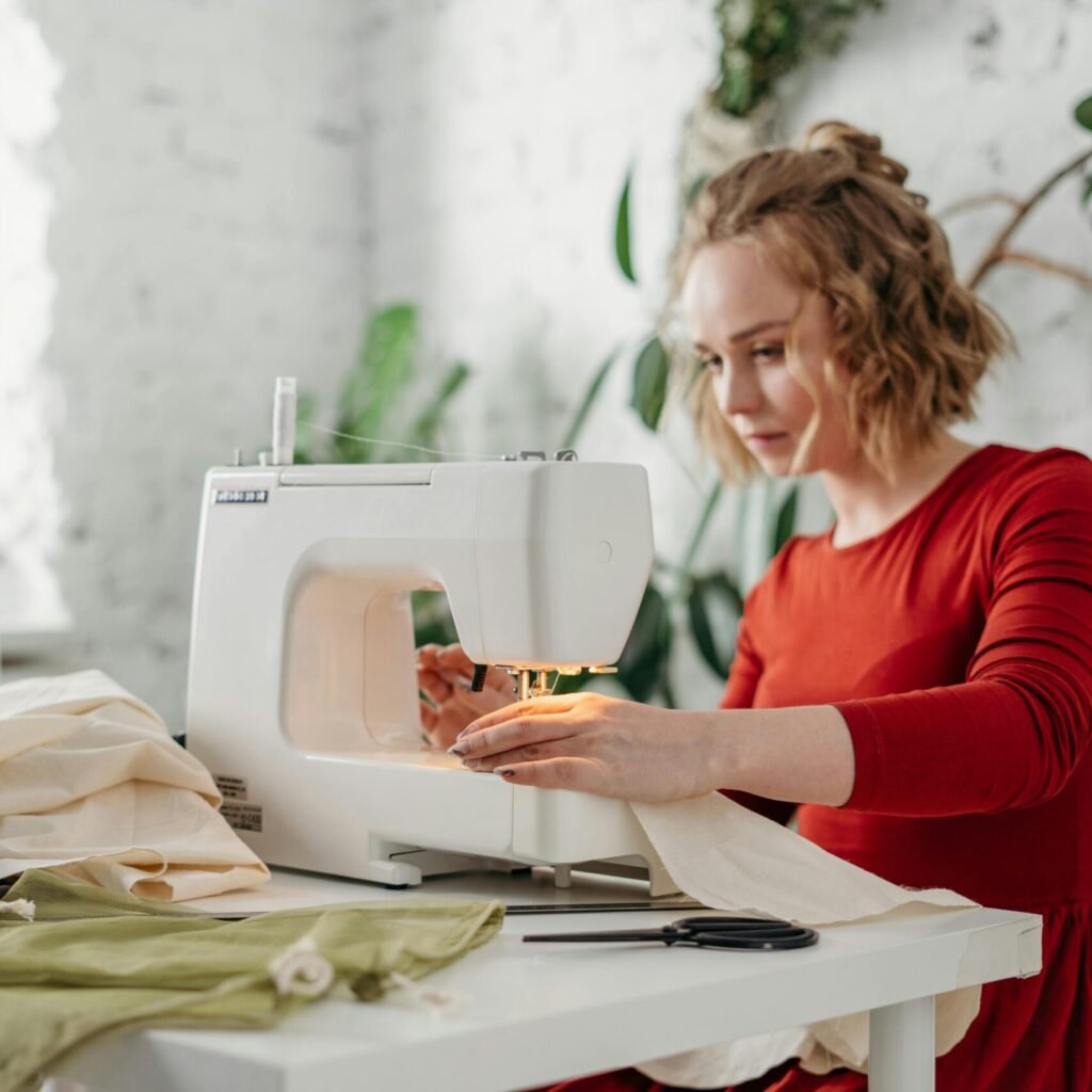 A woman in a red dress using a sewing machine at home, creating a handmade garment.