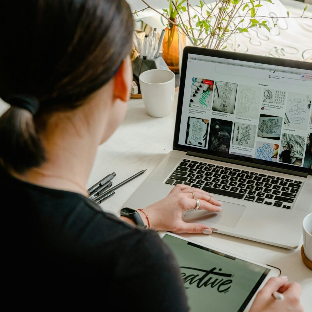 Woman in a creative workspace using a laptop and tablet for calligraphy. Artistic and tech-driven environment.