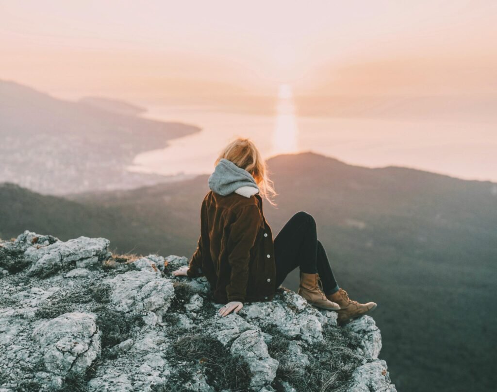 A woman sits on a rocky mountain enjoying the breathtaking sunrise view over the ocean.
