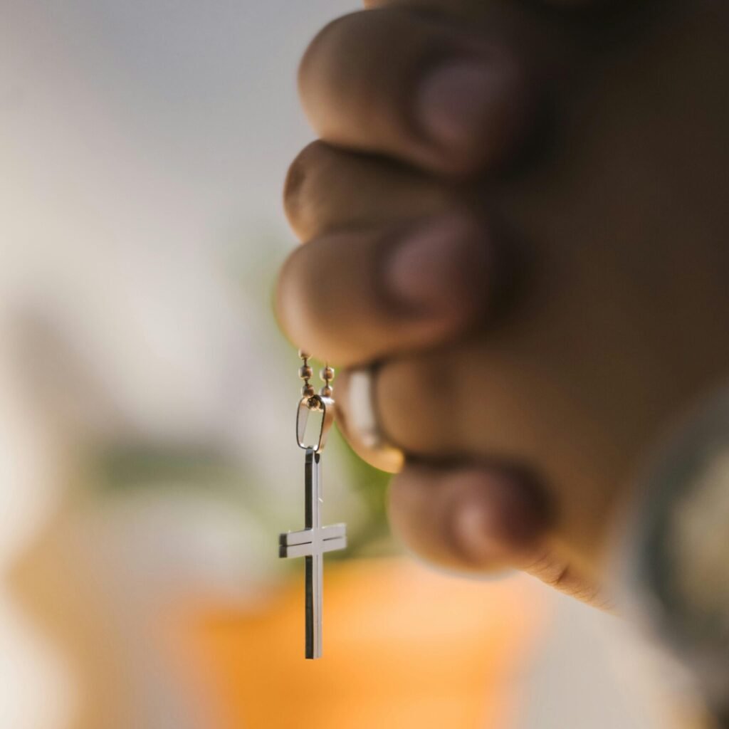 Close-up of hands clasped in prayer holding a cross pendant with blurred background.