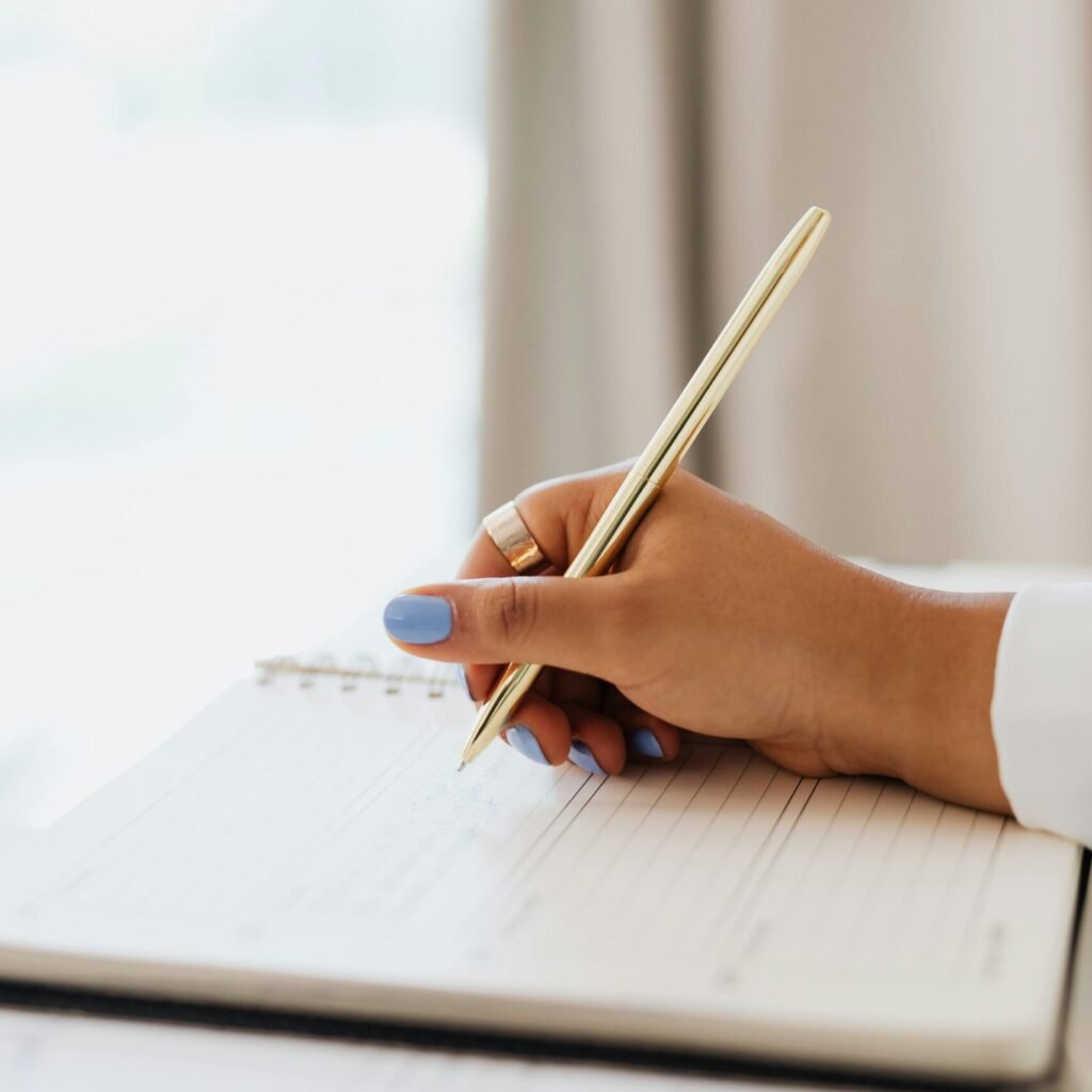Hand holding a pen poised over a lined notebook page, suggesting planning or journaling.