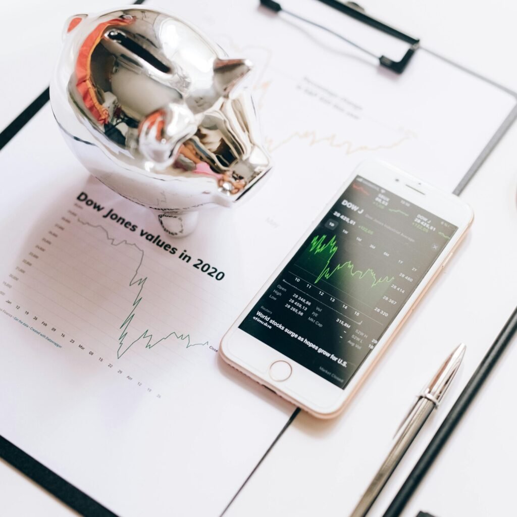 Flat lay of financial tools: chart, smartphone, magnifying glass, and piggy bank.