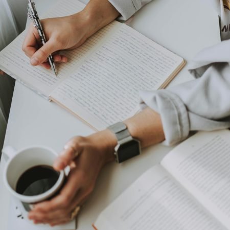 Close-up of a person writing in a notebook with coffee on a desk. Ideal for workplace or study themes.