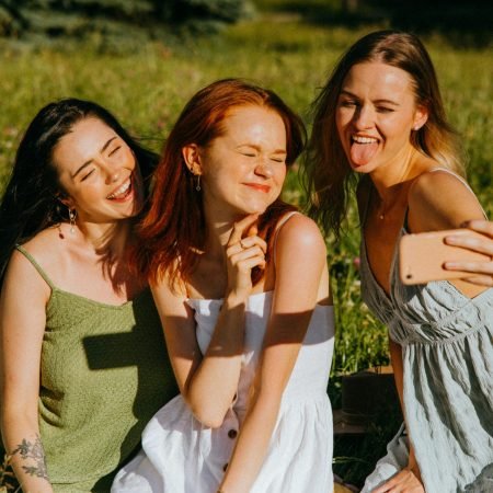 friends taking picture Three young women enjoying a cheerful selfie outdoors in a sunny park, capturing fun and friendship.